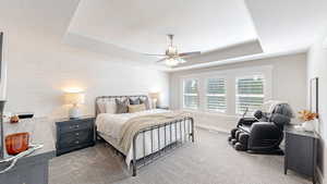 Carpeted bedroom featuring wood walls, a tray ceiling, baseboards, a textured ceiling, and a ceiling fan