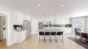 Kitchen featuring white cabinets, light wood-style flooring, appliances with stainless steel finishes, and a breakfast bar