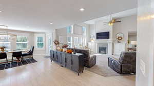 Living room with ceiling fan with notable chandelier, light wood-style floors, a glass covered fireplace, and a textured ceiling