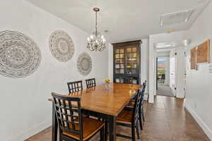 Tiled dining room with visible vents, a chandelier, and baseboards