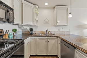 Kitchen featuring dark stone countertops, open shelves, a sink, black appliances, and decorative light fixtures