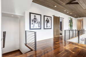 Hall with an upstairs landing, wood finished floors, a barn door, baseboards, and recessed lighting