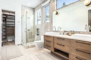 Bathroom with a shower stall, a walk in closet, double vanity, and toilet