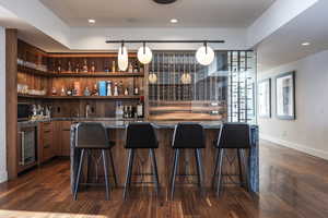 Indoor wet bar featuring wine cooler, black microwave, dark wood-style flooring, baseboards, and recessed lighting