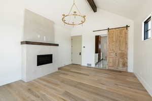 Unfurnished living room featuring beam ceiling, a chandelier, a barn door, wood finished floors, and visible vents
