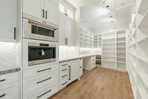 Kitchen featuring decorative backsplash, light wood finished floors, white cabinets, light stone countertops, and glass insert cabinets