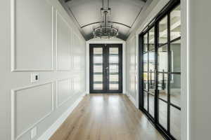 Doorway to outside featuring a decorative wall, an inviting chandelier, lofted ceiling, light wood-style floors, and french doors