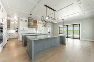 Kitchen featuring white cabinetry, a large island with sink, tasteful backsplash, coffered ceiling, and light wood-style floors