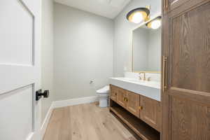 Half bathroom featuring toilet, vanity, baseboards, and wood finished floors