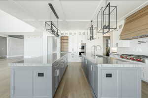 Kitchen featuring light wood-style flooring, premium range hood, appliances with stainless steel finishes, a sink, and a spacious island