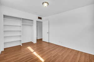 Unfurnished bedroom featuring a closet, baseboards, visible vents, and wood finished floors
