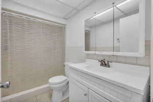Full bath featuring tile patterned floors, curtained shower, toilet, and tile walls