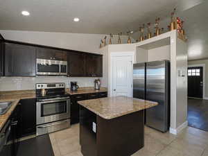 Kitchen with backsplash, light tile patterned floors, a kitchen island, and appliances with stainless steel finishes