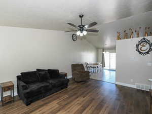Living room featuring lofted ceiling, dark wood-style flooring, a textured ceiling, ceiling fan, and visible vents