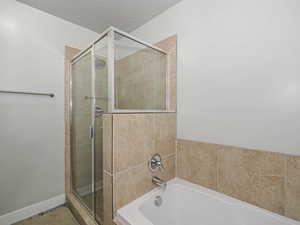 Bathroom featuring a stall shower, baseboards, a bath, and a textured ceiling