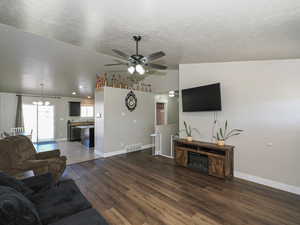 Living area featuring lofted ceiling, ceiling fan with notable chandelier, baseboards, visible vents, and wood finished floors