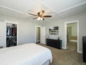 Carpeted bedroom with a closet, baseboards, ceiling fan, ensuite bath, and coffered ceiling