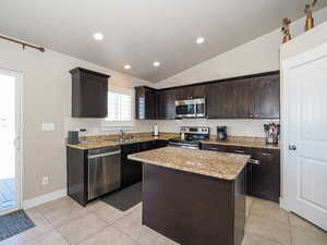 Kitchen featuring tasteful backsplash, lofted ceiling, stainless steel appliances, light tile patterned flooring, and dark brown cabinetry