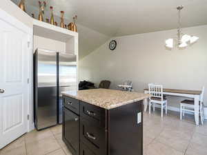 Kitchen with light countertops, a chandelier, vaulted ceiling, light tile patterned floors, and freestanding refrigerator