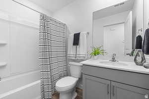 Bathroom featuring vanity, shower / tub combo, toilet, visible vents, and wood finished floors
