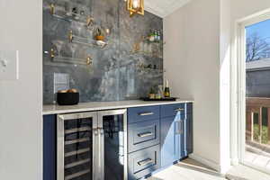 Dry bar in family room with soda/wine fridge and blue cabinets with tile backsplash