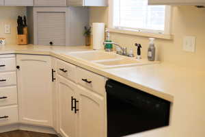 Kitchen with a sink, white cabinets, light countertops, and dishwasher