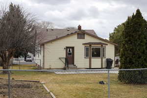 View of front facade with fence, entry steps, a front yard, a shingled roof, and a chimney