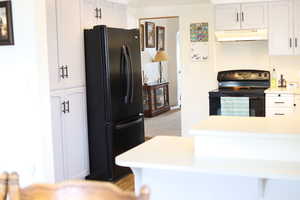 Kitchen with white cabinetry, light countertops, under cabinet range hood, and black appliances