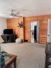 Living area with carpet floors, a textured ceiling, wooden walls, and a ceiling fan