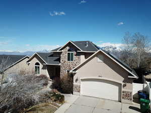 View of front facade with stone siding, a mountain view, concrete driveway, and stucco siding