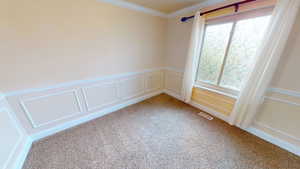 Unfurnished room featuring carpet, ornamental molding, a decorative wall, and wainscoting
