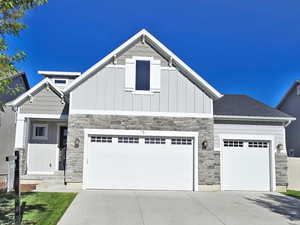Craftsman-style home with stone siding, board and batten siding, concrete driveway, and fence