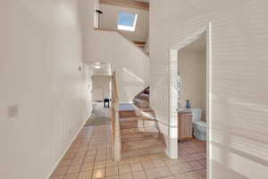 Staircase with baseboards, a towering ceiling, tile patterned flooring, and a skylight