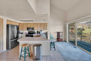 Kitchen with light countertops, a sink, a breakfast bar, light brown cabinetry, and stainless steel appliances