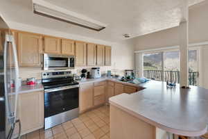 Kitchen with light countertops, a peninsula, stainless steel appliances, light brown cabinets, and light tile patterned floors