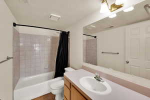 Full bath featuring a textured ceiling, visible vents, toilet, vanity, and shower / tub combo with curtain