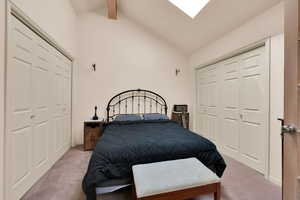 Carpeted bedroom with high vaulted ceiling, a closet, a skylight, and beamed ceiling