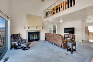 Carpeted living area with a high ceiling, visible vents, a healthy amount of sunlight, and a tile fireplace