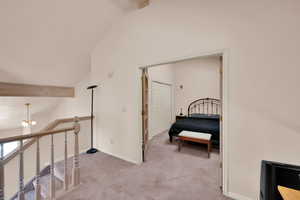 Corridor with an upstairs landing, light carpet, lofted ceiling with beams, baseboards, and an inviting chandelier