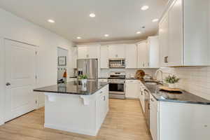 Kitchen featuring white cabinetry, stainless steel appliances, a kitchen island, a sink, and light wood-style floors