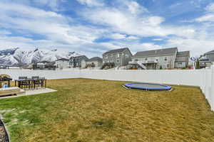 View of yard featuring a trampoline, a fenced backyard, a residential view, a patio, and a mountain view