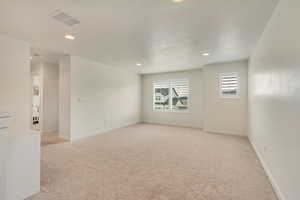 Empty room with baseboards, visible vents, recessed lighting, and light carpet