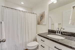 Full bath with curtained shower, toilet, recessed lighting, and vanity