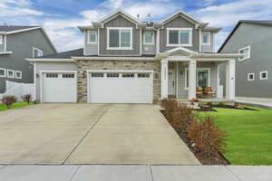 View of front of house with covered porch, concrete driveway, board and batten siding, a garage, and stone siding