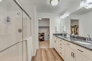 Full bathroom featuring double vanity, a sink, a shower stall, and wood finished floors