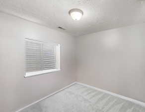Carpeted empty room with baseboards, visible vents, and a textured ceiling