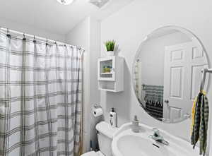 Bathroom with toilet, a sink, a shower with shower curtain, and visible vents