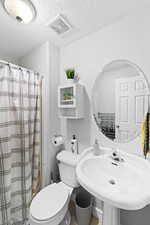 Full bathroom featuring toilet, a shower with shower curtain, a textured ceiling, a sink, and visible vents