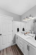 Bathroom with double vanity, a sink, toilet, and wood finished floors