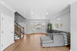 Living room with ornamental molding, stairway, and light wood-type flooring